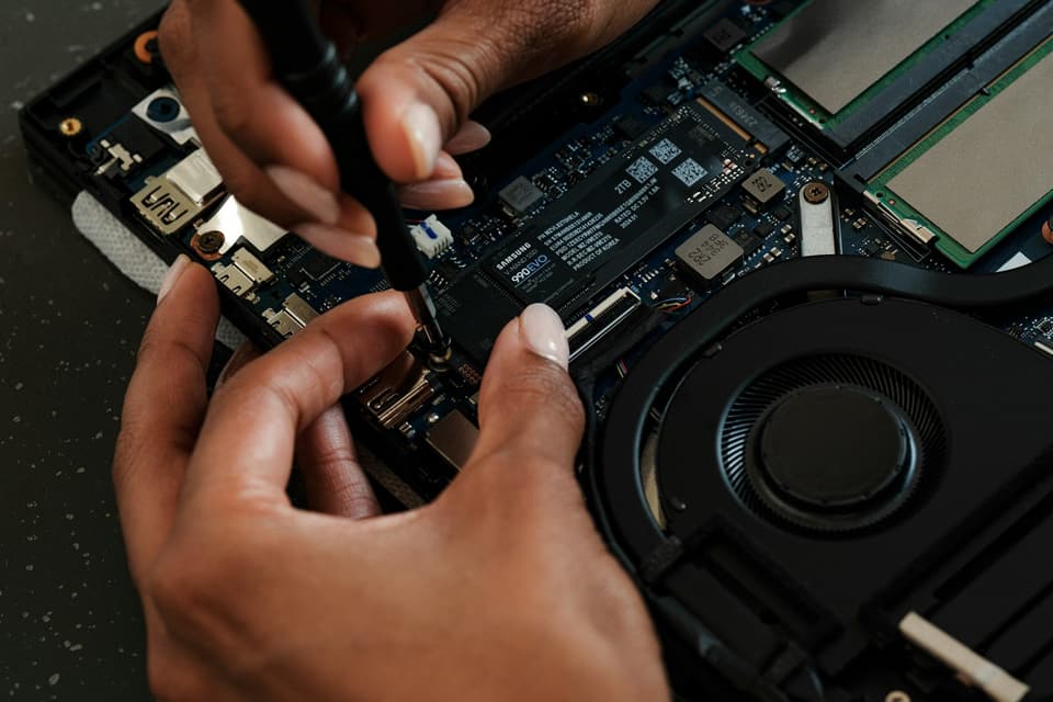 Mani al lavoro su un portatile aperto, con SSD e ventola in vista
