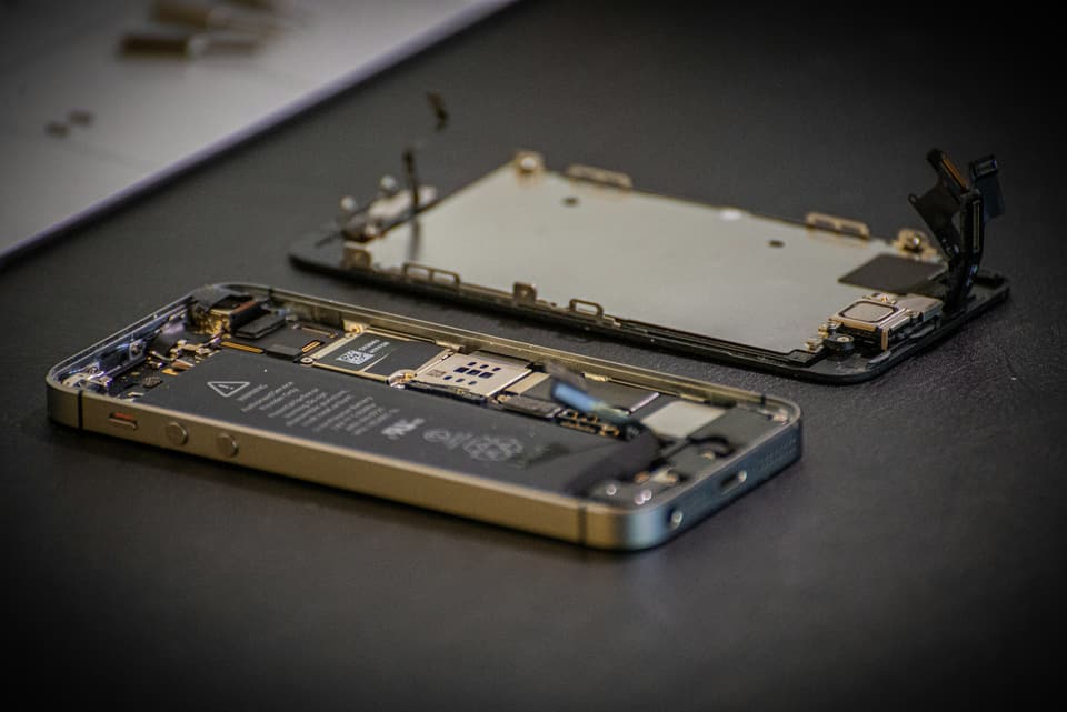 iPhone aperto sul banco: display sollevato, batteria e scheda in vista