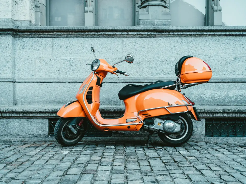 Scooter arancione parcheggiato su un marciapiede in pietra