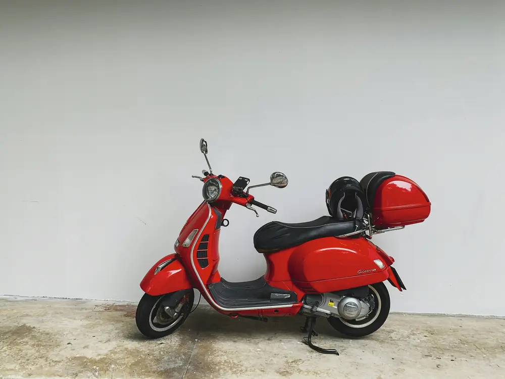 Scooter rosso con bauletto davanti a un muro bianco