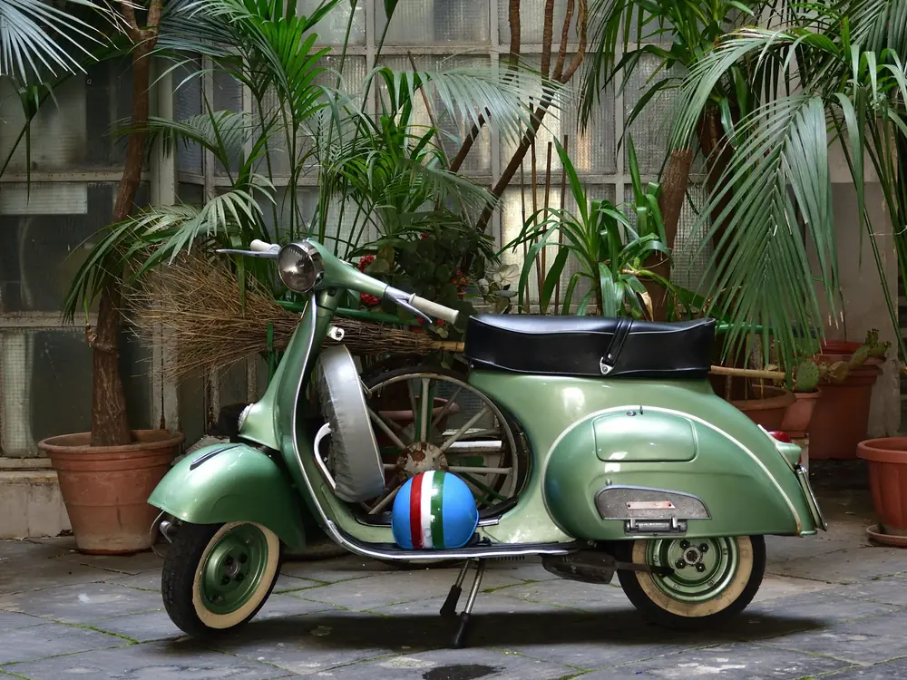 Scooter d'epoca verde tra le piante di un cortile