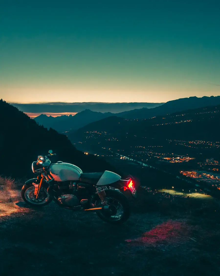 Moto café racer ferma su un belvedere di sera, luci della valle sotto