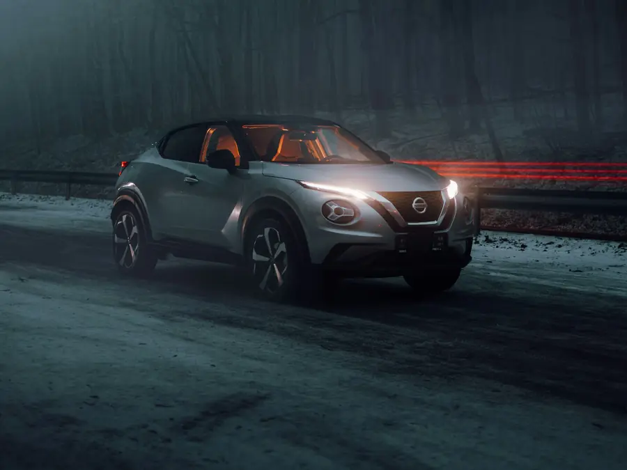 Nissan Juke grigia con i fari accesi su una strada nel bosco