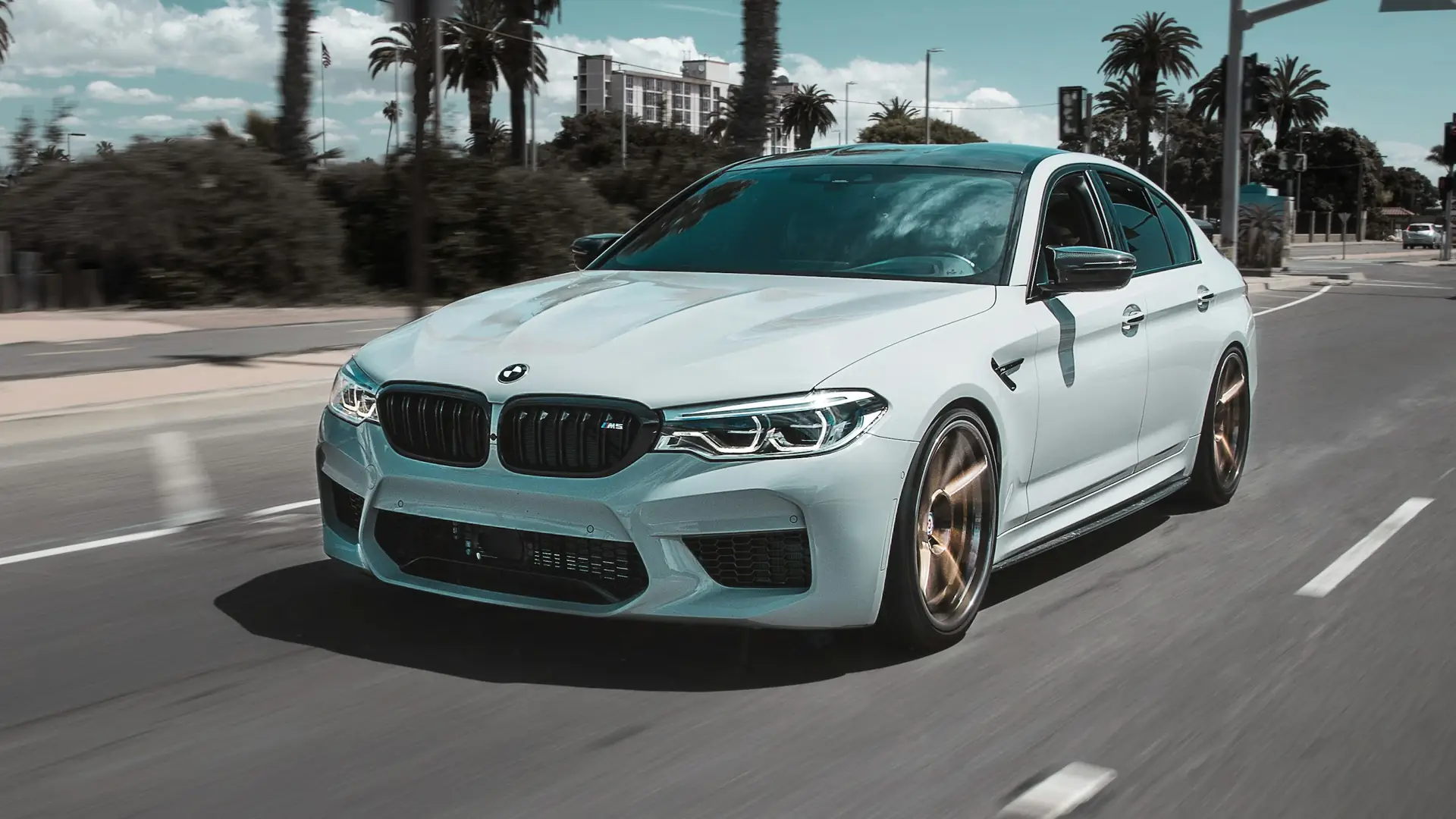 BMW berlina grigio chiaro in movimento su un viale