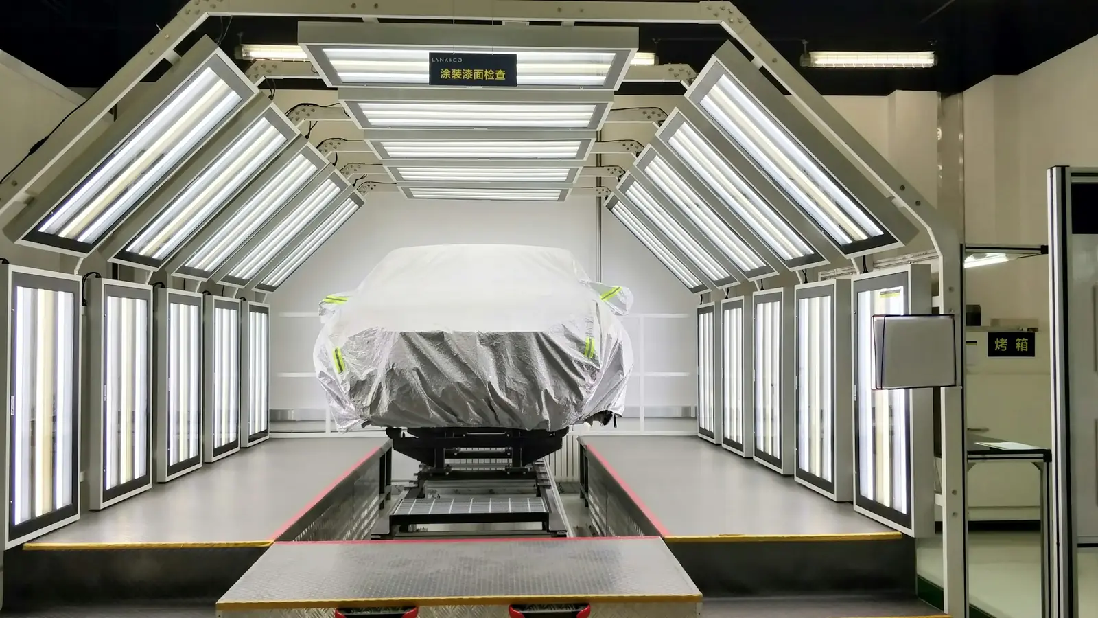 Cabina di verniciatura illuminata con un'auto coperta sul ponte