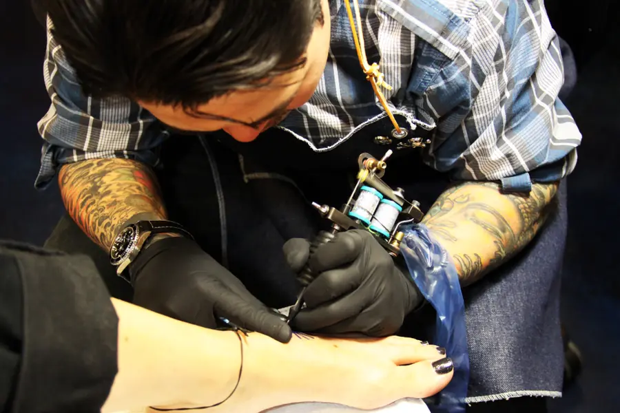 Tatuaggio sulla caviglia, mani con i guanti