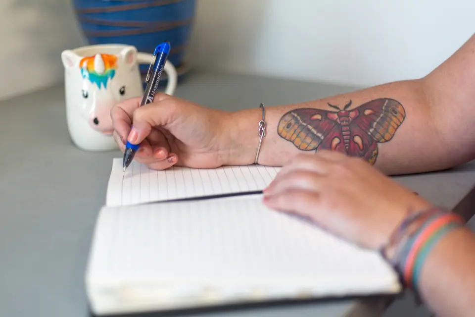 Mano con tatuaggio di falena che disegna su un quaderno