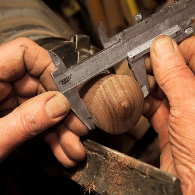 Mani che misurano un pomello di legno con il calibro