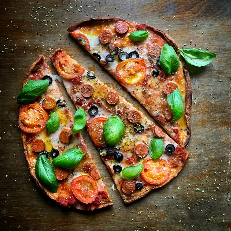 Pizza tagliata a spicchi con pomodori, olive e basilico