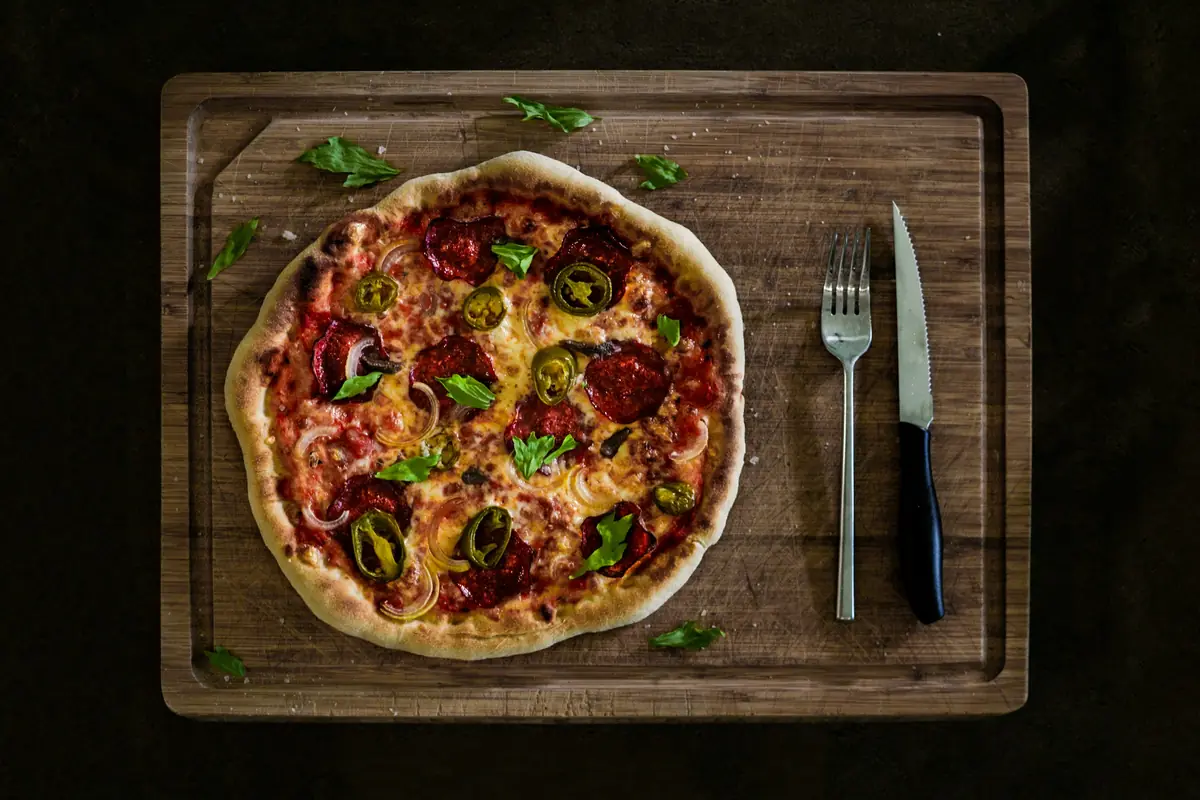 Pizza servita su tagliere con coltello e forchetta