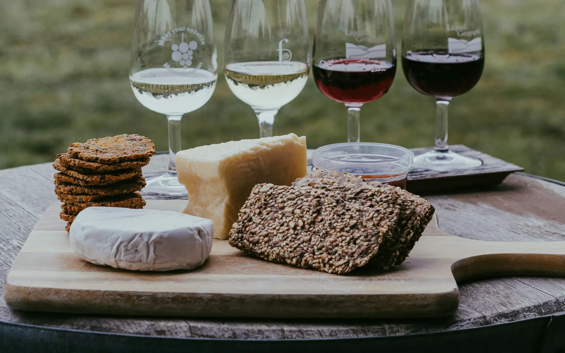 Quattro calici di vino e formaggi su un tavolino in mezzo alla vigna