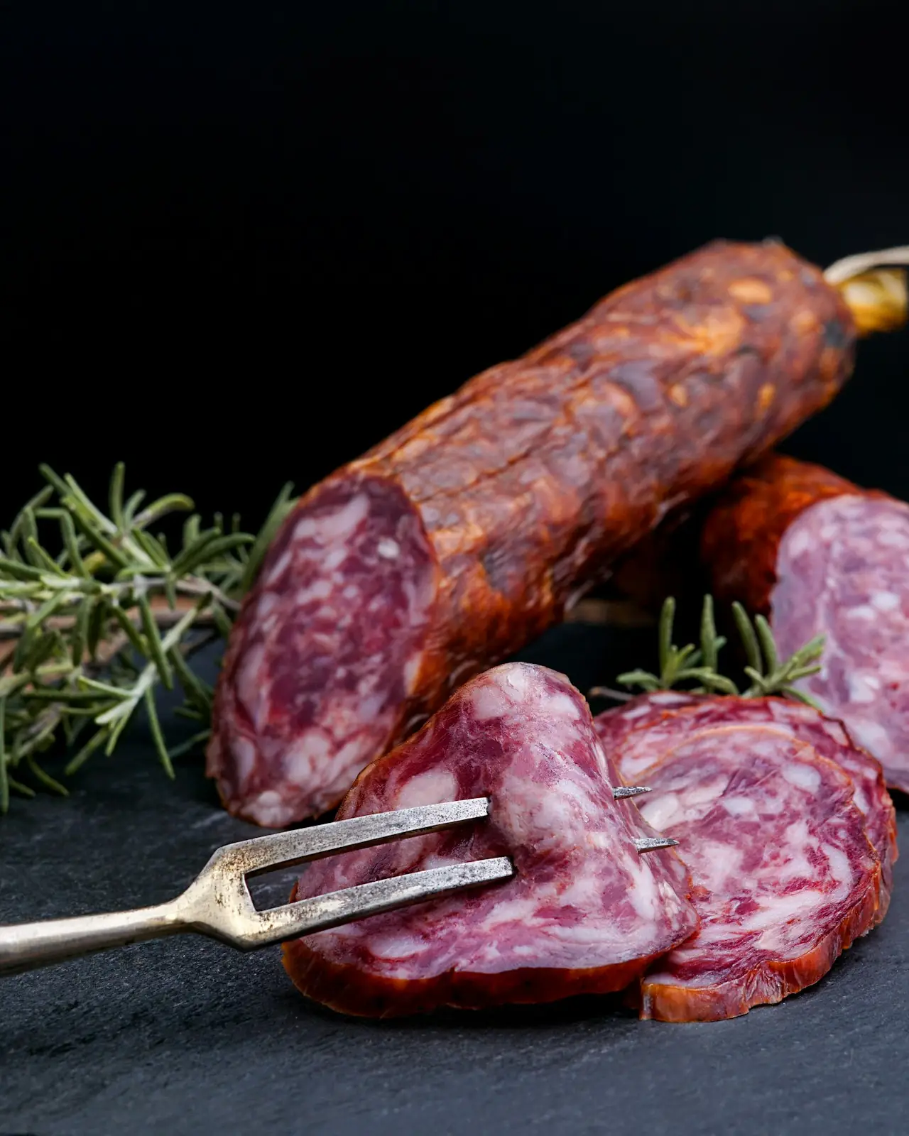 Salame tagliato a fette sul tagliere con il rosmarino
