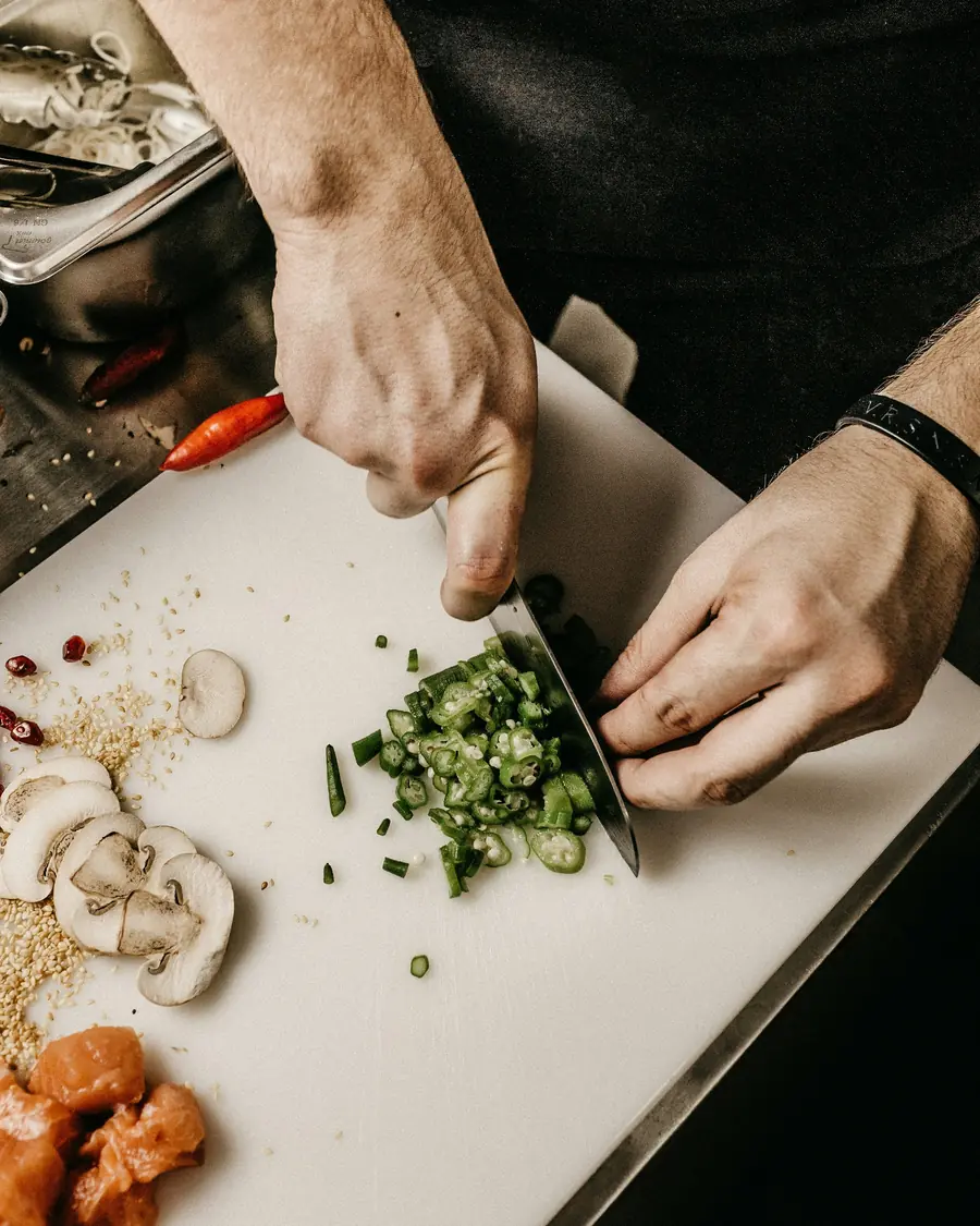 Mani che tagliano erba cipollina col coltello sul tagliere