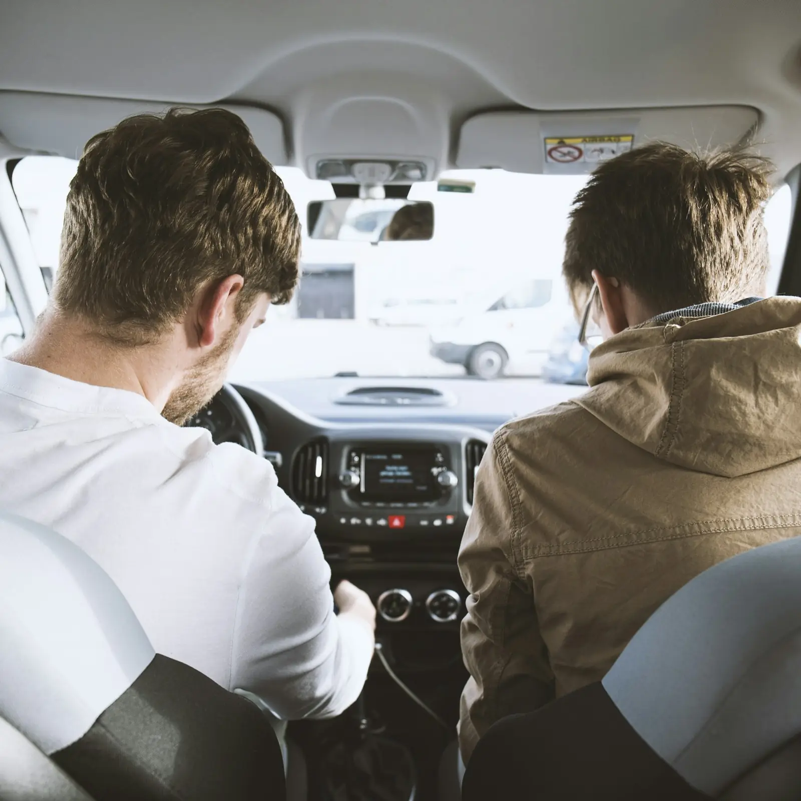 Istruttore e allievo seduti davanti in un'auto con doppi comandi, visti dal sedile posteriore