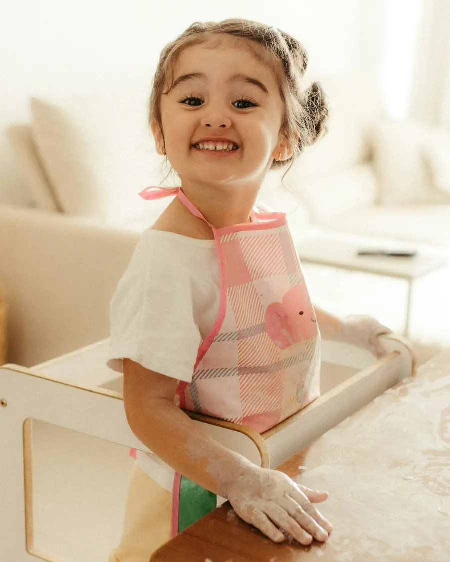 Bambina col grembiule che impasta in cucina e sorride