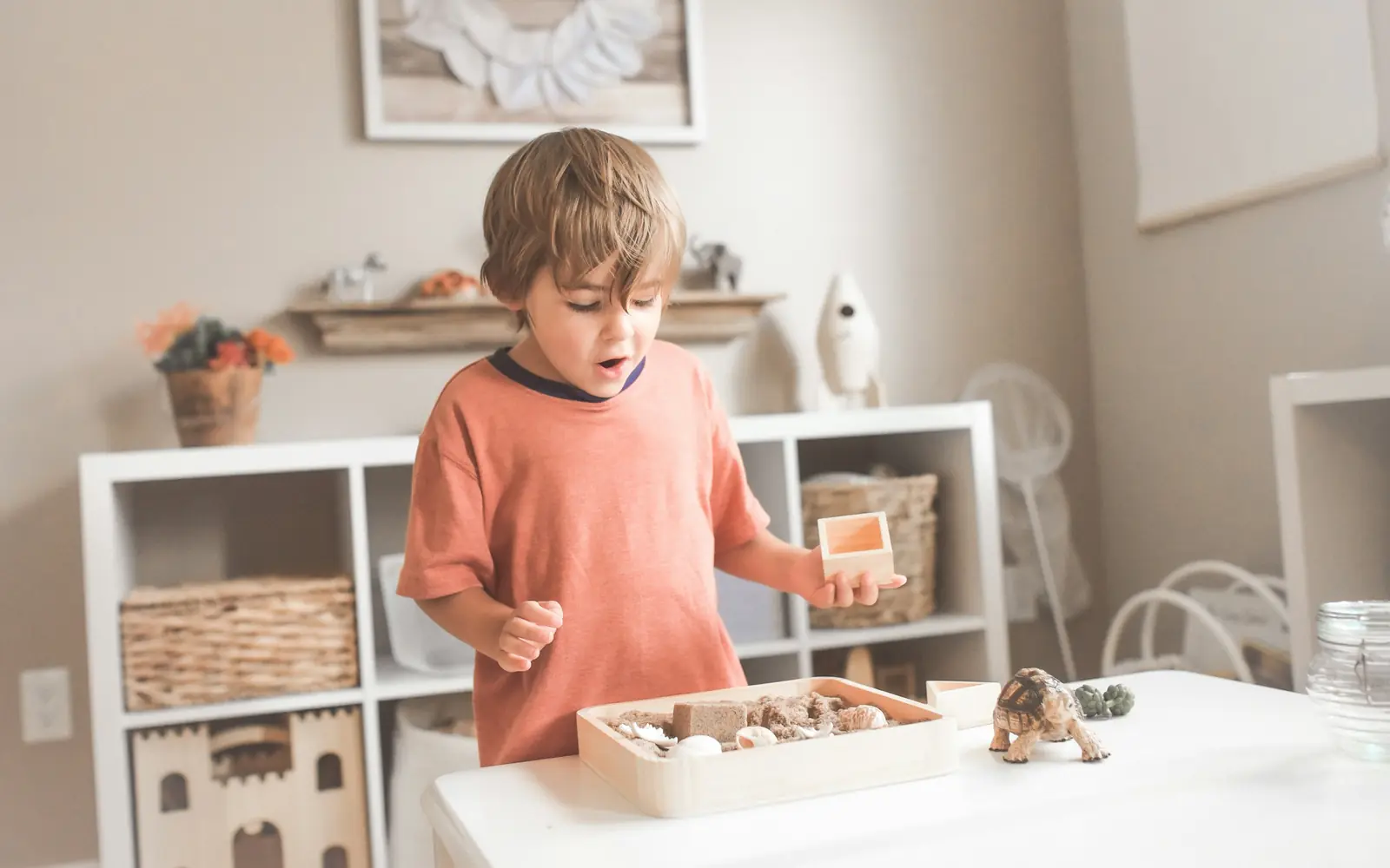 Bambino al tavolino che gioca con i materiali in legno, scaffali di giochi alle spalle