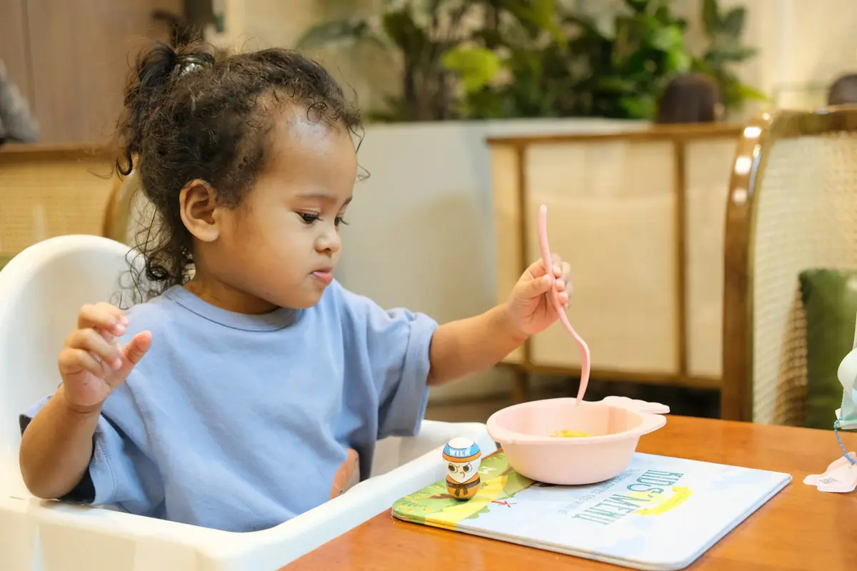 Bimba sul seggiolone che mangia la pasta con la forchetta
