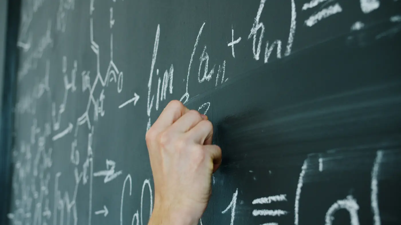 Mano che scrive formule col gesso su una lavagna