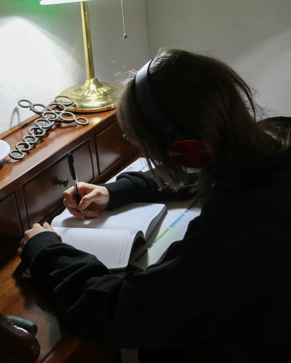 Ragazza che scrive sul quaderno sotto una lampada da tavolo verde