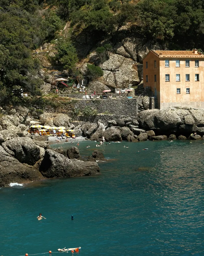 Caletta di scogli con acqua trasparente e una casa sul promontorio