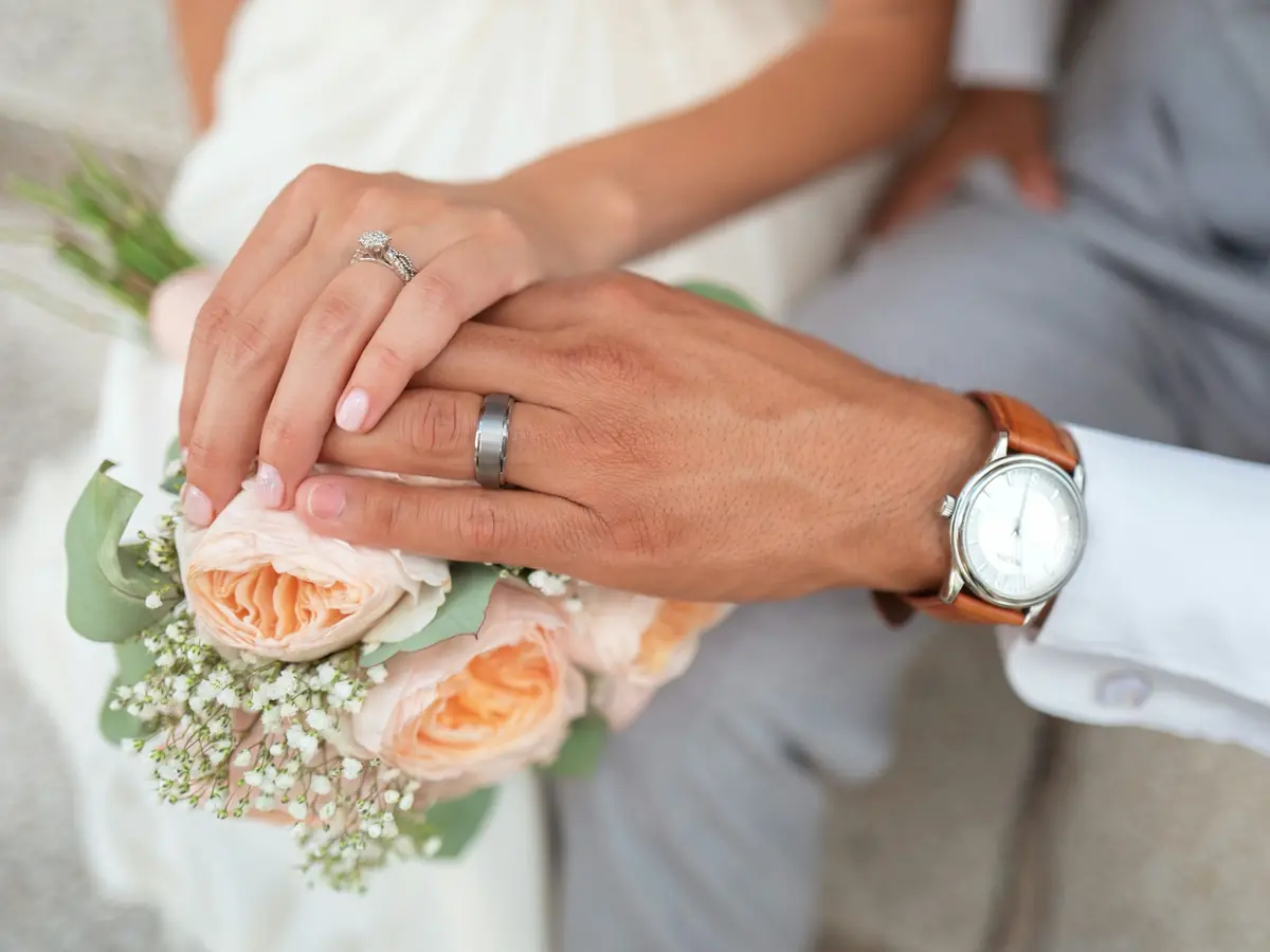 Mani degli sposi con il bouquet di rose pesca