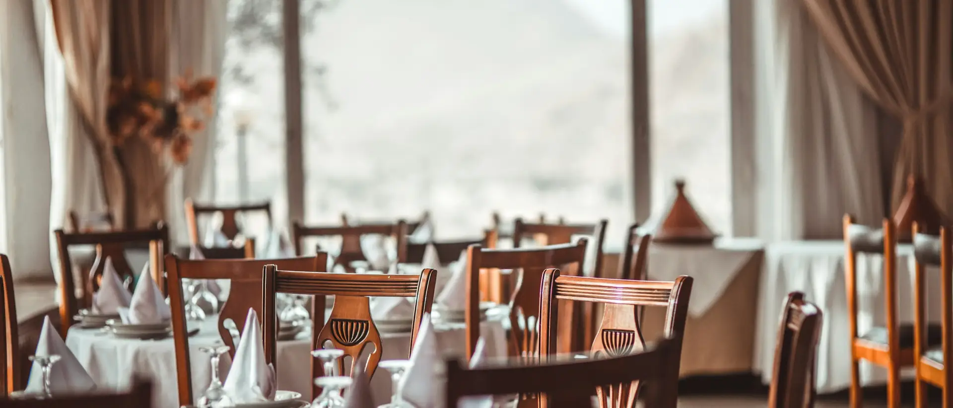 Sala del ristorante con tavoli apparecchiati e vetrate sulle montagne