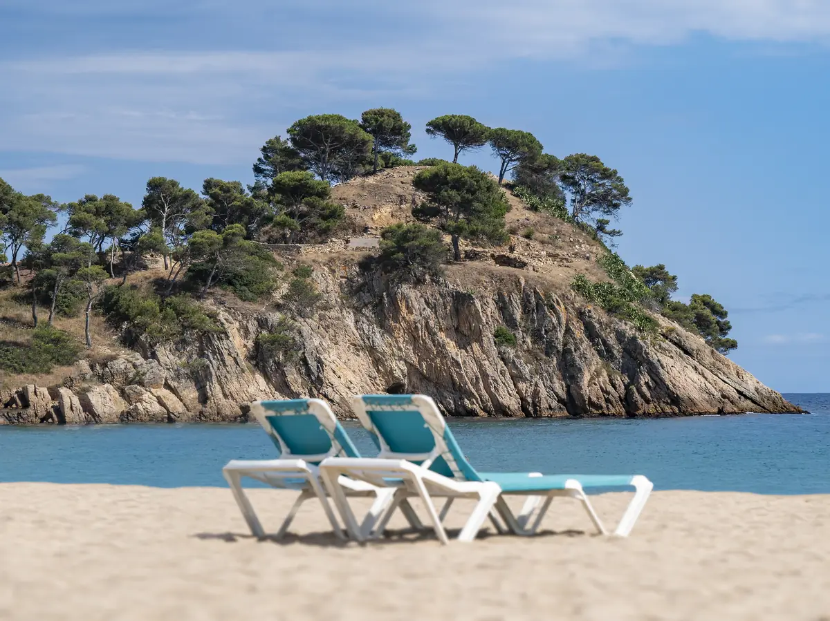 Spiaggia con due sdraio e il promontorio coperto di pini