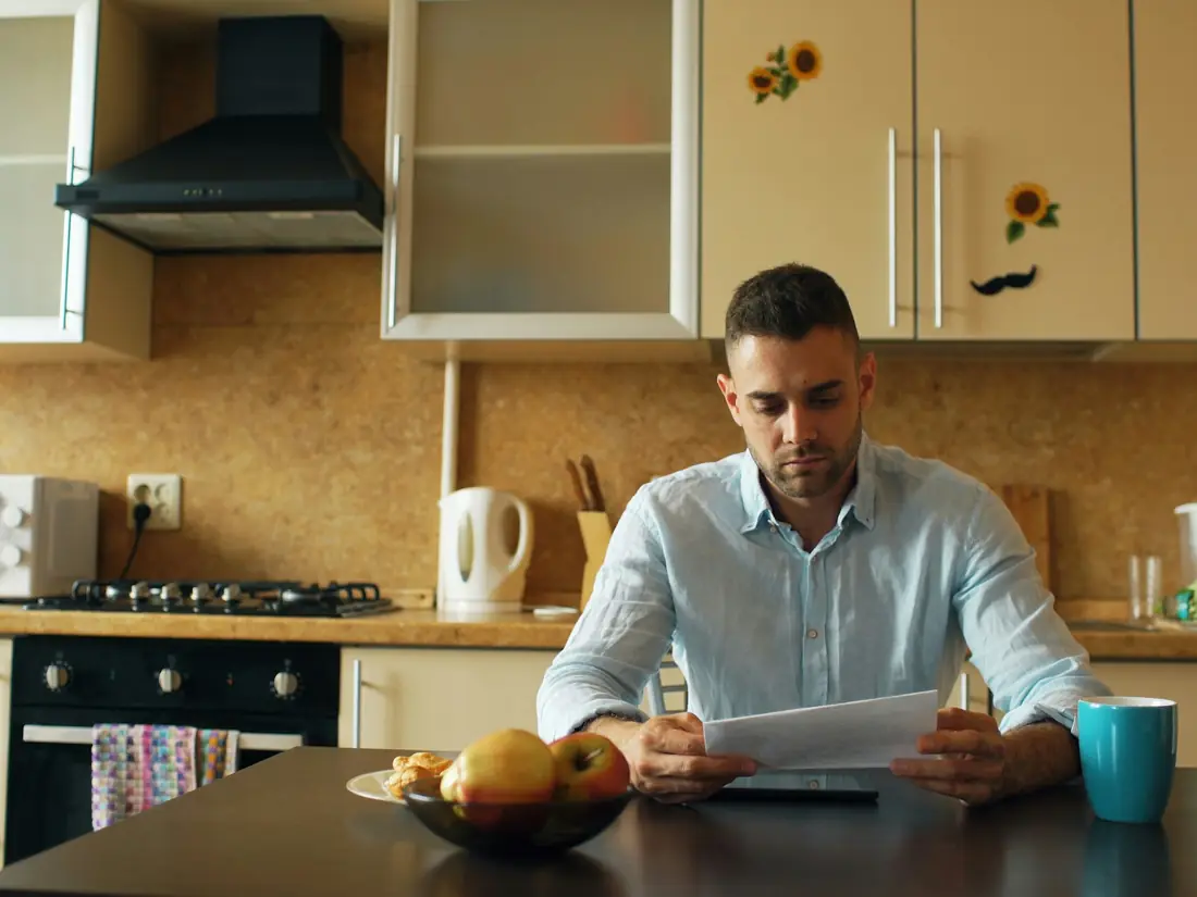 Un uomo legge dei documenti al tavolo della cucina