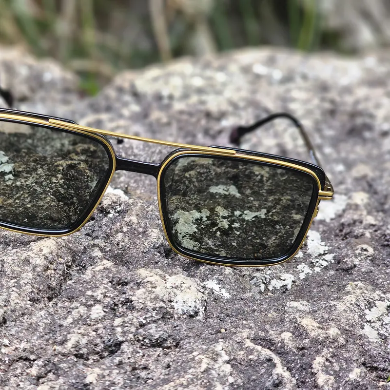 Occhiale da sole squadrato in metallo dorato su una roccia