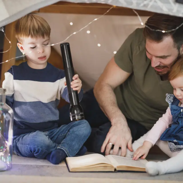 Un adulto legge una storia a due bambini in una tenda di coperte