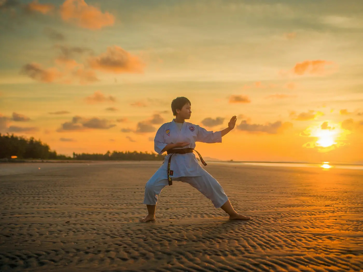 Ragazzo in karategi che esegue un kata sulla spiaggia al tramonto