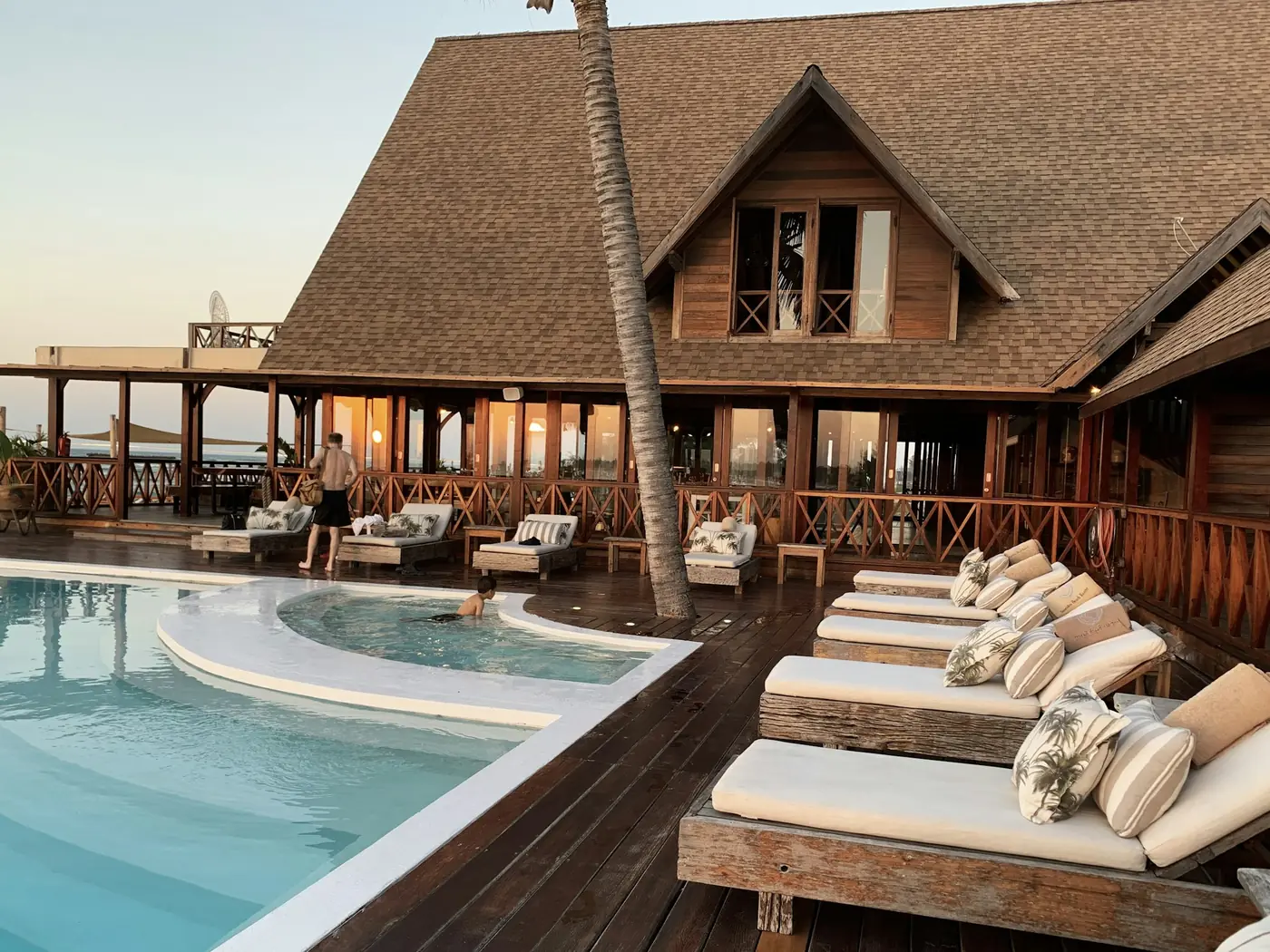 Piscina e lettini davanti a un hotel in legno al tramonto